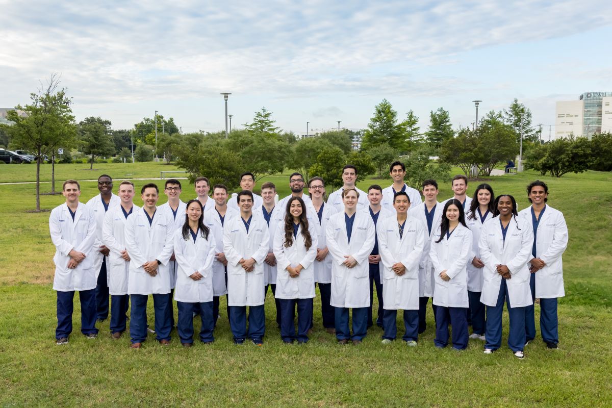 group of 30 Orthopaedic Surgery Residents in white coats and blue scrubs standing outside hospital